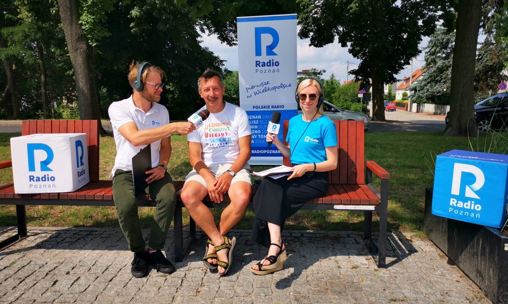 Andrzej Surdyk wraz z dwoma redaktorami siedzą na ławce na terenie dworca PKP w Skokach 