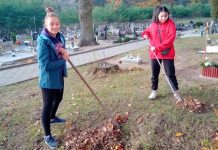 2 uczennice grabią liście na cmentarzu