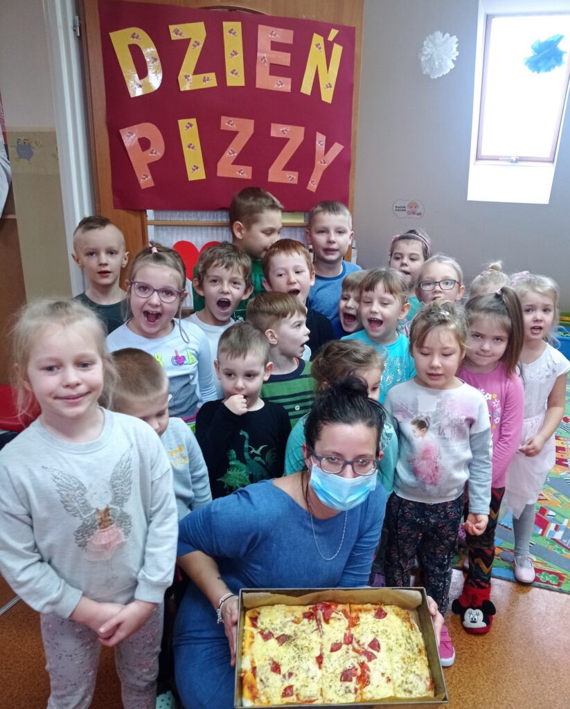 Uśmiechnięta grupa dzieci z nauczycielką i upieczoną pizzą 