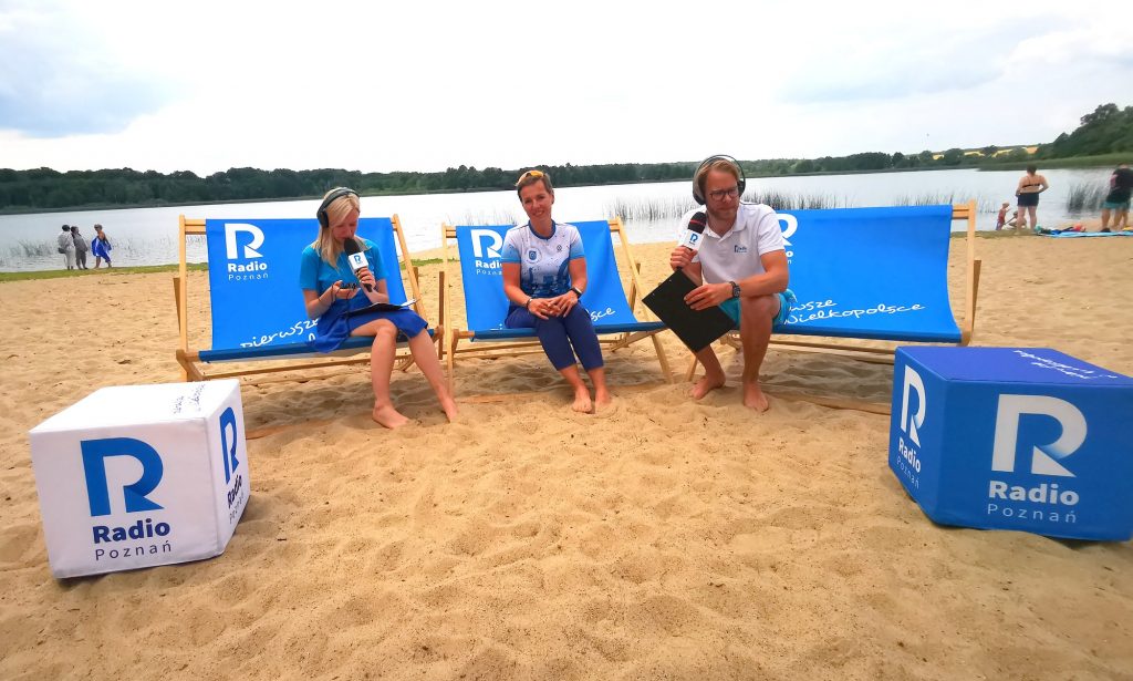 Karolina Stefaniak wraz z dwoma redaktorami siedzą na leżakach plażowych na plaży jeziora Włókna 
