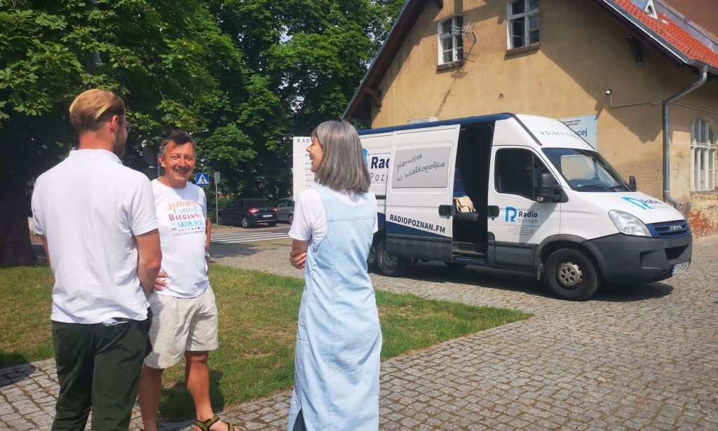 Andrzej Surdyk rozmawia z 2 redaktorami na tle budynku dworca PKP w Skokach 