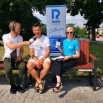 Andrzej Surdyk wraz z dwoma redaktorami siedzą na ławce na terenie dworca PKP w Skokach