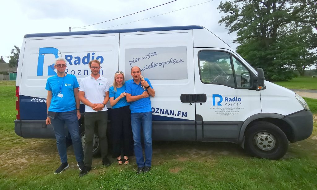 4 redaktorów radiowych na tle wozu transmisyjnego 