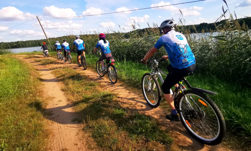 6 rowerzystów jedzie drogą przez stawy rybne w Skokach 