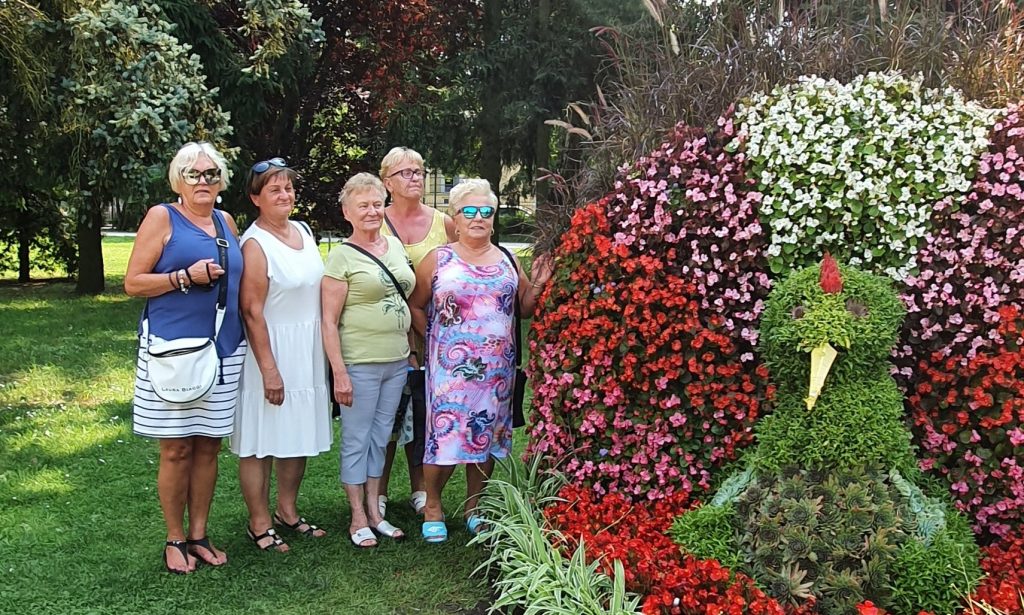 5 pań stoi w parku przy kompozycji kwiatowej w kształcie ptaka 