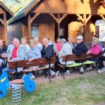 uczestnicy wjazdu siedzą przy długim stole na tle domków kempingowych