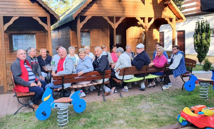uczestnicy wjazdu siedzą przy długim stole na tle domków kempingowych