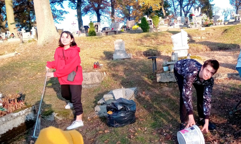 2 uczennice grabią liście na cmentarzu