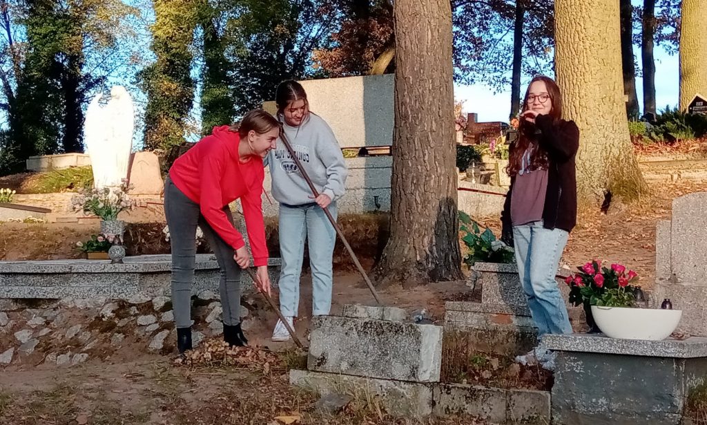 3 uczennice grabią liście na cmentarzu